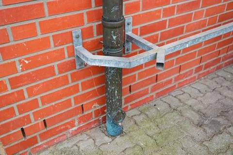 Metal pipe support bracket attached to red brick wall on paved ground outdoor Stock Photos
