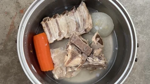 Metal pot with boiled pork bones, carrot and onion in water  Vídeo Stock 342438272