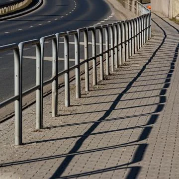 Metal railing casting shadows along curved roadside walkway Stock Photos