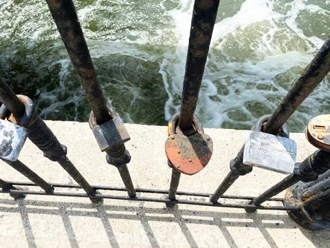 Metal railing with various padlocks attached, overlooking flowing water Stock Photos