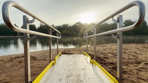 A metal ramp extends toward calm lake water on a sandy beach in Pushkin Video stock 344980236