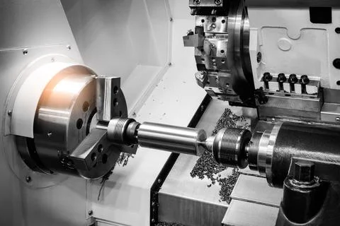 Metal rod spins precisely between lathe chuck jaws. Fine metal shavings fly f Foto stock