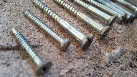 Metal screws arranged on a rough surface. Steel fasteners for construction and Stock Photos