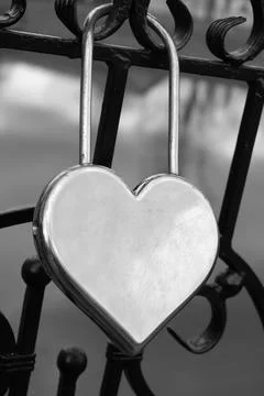 Metal silver door lock in the shape of a heart on the fence as a symbol of Stock Photos