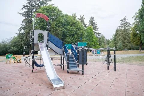 A metal slide and climbing structure on a rubber-tiled playground with trees  Stock Photos
