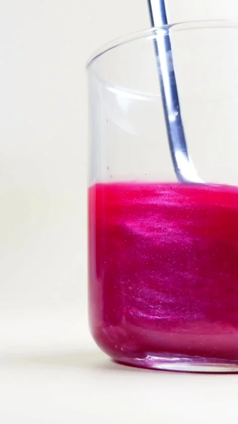 Metal spoon stirs vibrant pink pearlescent liquid in glass Stock Footage 331774792