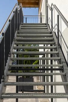 A metal staircase with open risers ascends to a building's entrance. Sunlig.. Stock Photos