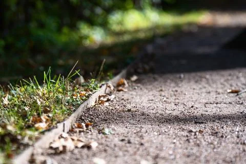 A metal strip divider separating a paved pathway from the green lawn grass Stock Photos