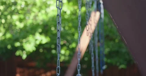 Metal swing set chains sway gently against a lush green background Stock Footage 326692793