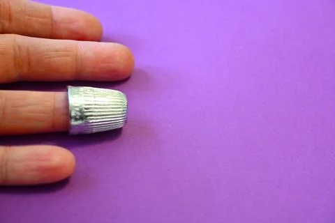 Metal thimble on finger purple background with copy space Fotos Stock