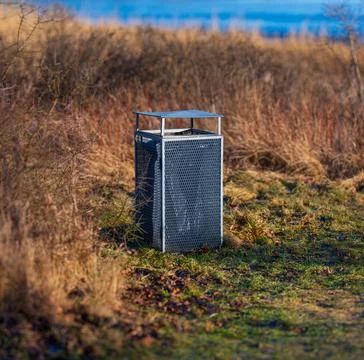 Metal trash bin in grassy field near water Stock Photos