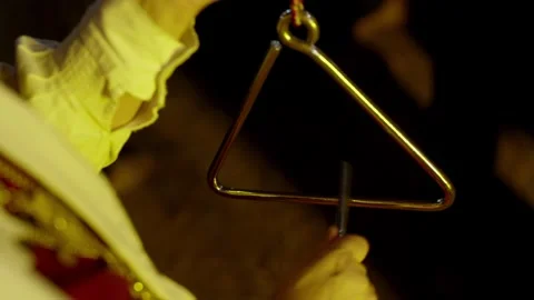 Metal triangle percussion instrument held close up in warm light Video stock 344512197