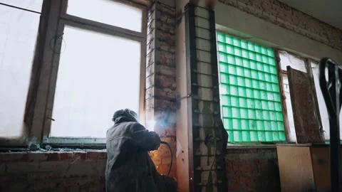 A metal welder welds metal structures near a window on a wall in a warehouse Stock Footage 264071380