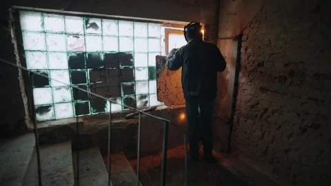 A metal welder welds metal structures near a window on a wall in a warehouse. A Stock Footage 264126092
