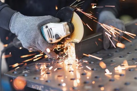 A metal worker cuts a rectangular metal pipe with an angle grinder Foto stock