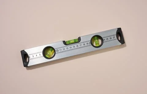Metallic building level on a beige background. Measuring instrument Stock Photos