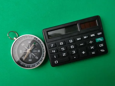 A metallic compass placed alongside a compact black pocket calculator on a .. Stock Photos