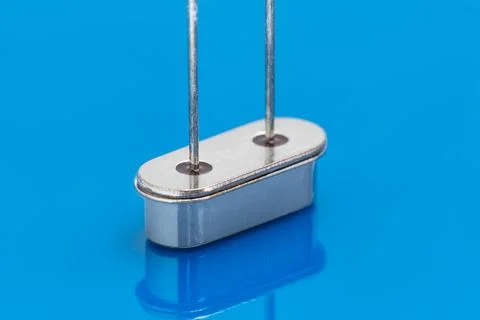 Metallic component with two vertical pins stands on reflective blue surface Stock Photos