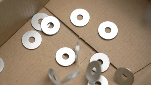 Metallic fastener washers falling into a cardboard box Stock Footage 283582049