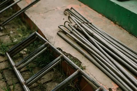 Metallic frames and rods lie on textured concrete in outdoor setting Stock-Fotos