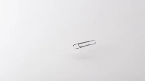 Metallic paperclips dropping onto a white surface in slow motion Stock Footage 117349906