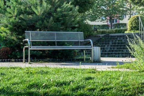 A metallic park bench surrounded by greenery near a staircase in a sunny outdoor Stock Photos