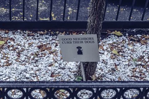 A Metallic sign at base of sidewalk tree stating that good neighbors curb their Stock Photos