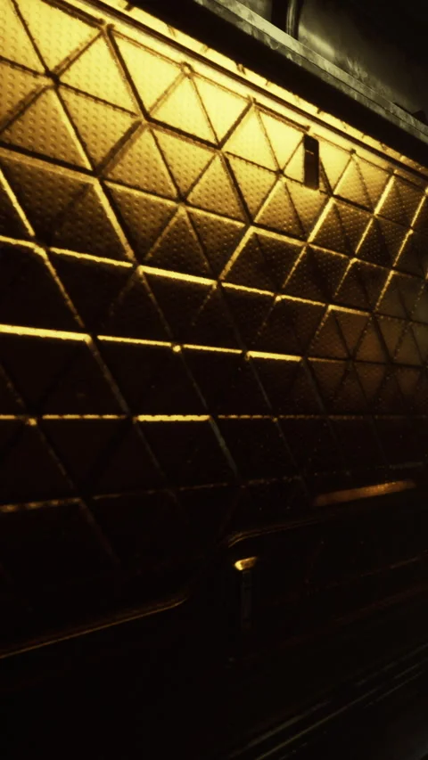 Metallic wall with diamond pattern reflecting warm light in dark setting Stock Footage 337972770