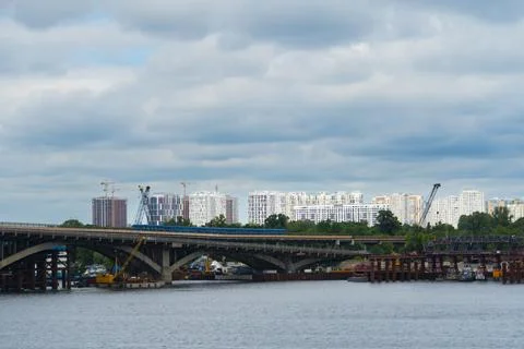 Metro train on bridge over river with city skyline and construction cranes Stock Photos