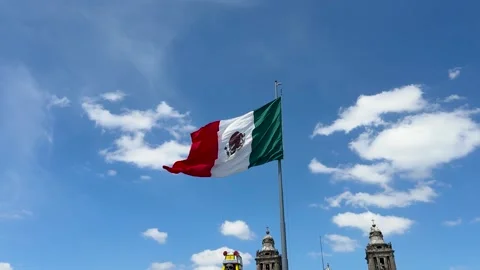 Mexican flag captured fluttering in the wind on a sunny urban day Видео 321813129