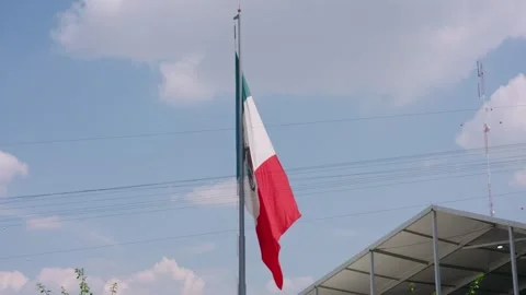 Mexican flag waving on a flagpole under a blue sky with white clouds 動画素材 340913258
