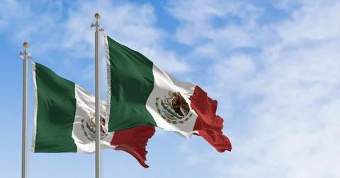 Mexican flags with its coat of arms waving against a blue sky. Stock Photos