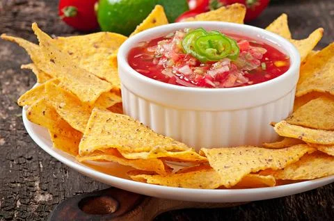 Mexican nacho chips and salsa dip in bowl on wooden background Stock Photos