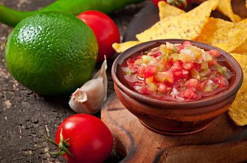 Mexican nacho chips and salsa dip in bowl on wooden background Stock Photos
