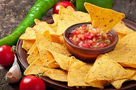 Mexican nacho chips and salsa dip in bowl on wooden background Stock Photos