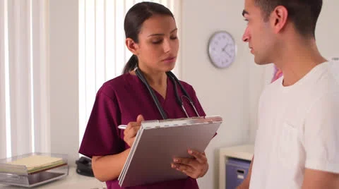 Mexican nurse writing notes while talking to patient Stock-Footage 25629398