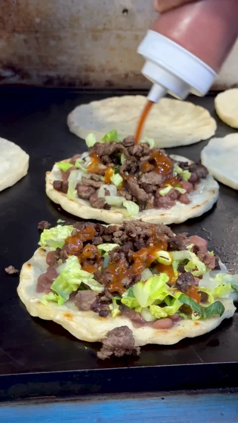 Mexican sopes with beans, beef, and lettuce cooking on flat top grill 库存影片 330269840