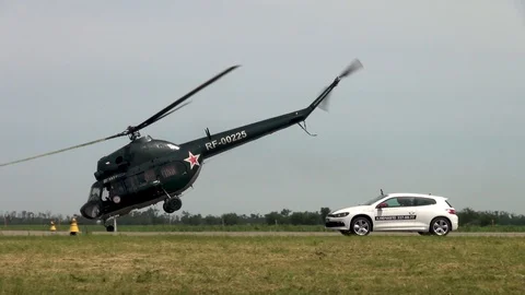 Mi-2 helicopter flies low over runway and car of Jaguar begins to accelerate. Stock Footage 121203515