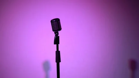 A mic comes out of dark in the light of spotlight on multi color background. Stock Footage 118527329