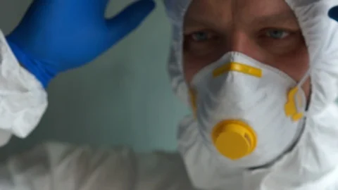 Microbiologist in a protective suit puts on a mask and takes a tube with a Stock Footage 129333158