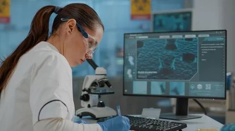 Microbiologist taking notes on paper and analyzing dna on computer 스톡 사진