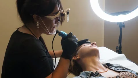 Microblading artist works under ring light as client undergoes beauty ritual of Stock Footage 307494944