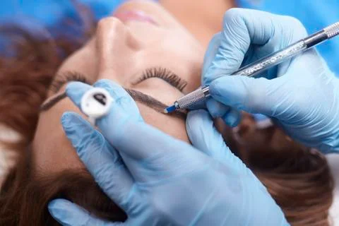 Microblading close-up, hands adding pigment to eyebrows. Stock Photos
