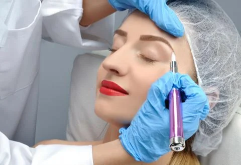 Microblading eyebrows. Cosmetologist making permanent makeup. Attractive woma Фото