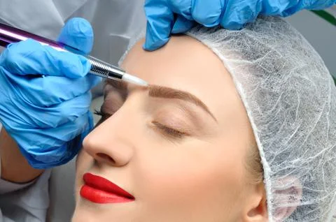 Microblading eyebrows. Cosmetologist making permanent makeup. Attractive woma Stock Photos