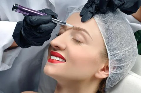 Microblading eyebrows. Cosmetologist making permanent makeup. Attractive woma Stock Photos