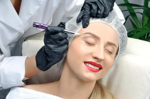 Microblading eyebrows. Cosmetologist making permanent makeup. Attractive woma Stock Photos