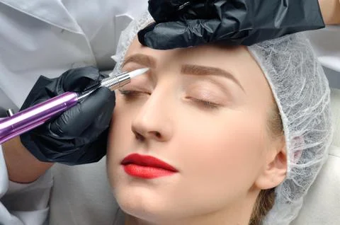 Microblading eyebrows. Cosmetologist making permanent makeup. Attractive woma Фото
