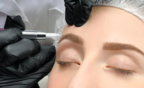 Microblading eyebrows. Cosmetologist making permanent makeup. Attractive woma Stock Photos