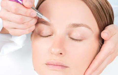 Microblading eyebrows. Cosmetologist making permanent makeup. Attractive woma Stock Photos